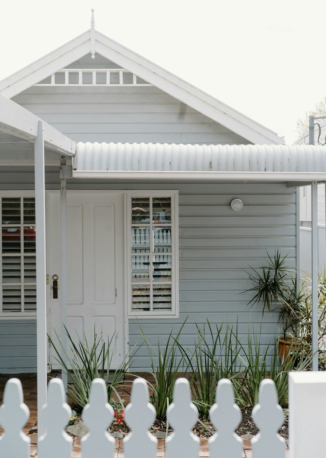 White weatherboard cottage in Sydney with a picket fence and established garden